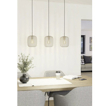 Drie metalen hanglampen boven een eettafel met decoratie en stoelen.