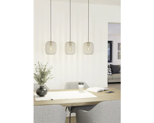 Drie metalen hanglampen boven een eettafel met decoratie en stoelen.