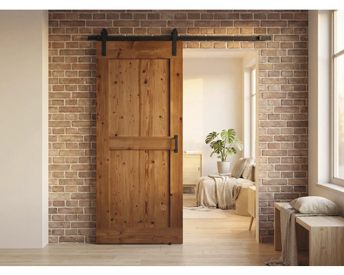 Houten schuifdeur voor een bakstenen muur met een woonruimte op de achtergrond.