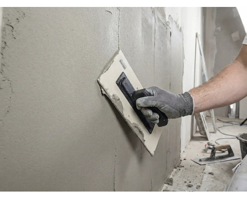 Ambachtsman egaliseert muur met een pleisterspaan en vulmiddel.