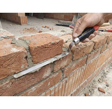 Ambachtsman bewerkt bakstenen muur met voegspijker