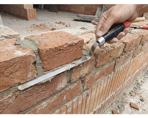 Ambachtsman bewerkt bakstenen muur met voegspijker