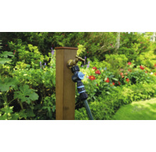 Tuinscene met waterkraan, verdeler en slang op een houten paal