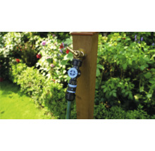 Tuinscene met waterkraan aan houten paal en aangesloten tuinslang