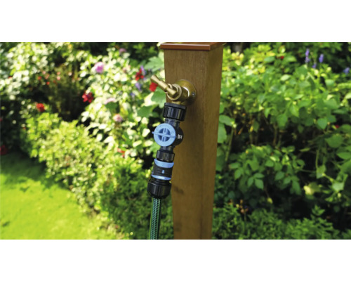 Tuinscene met waterkraan aan houten paal en aangesloten tuinslang