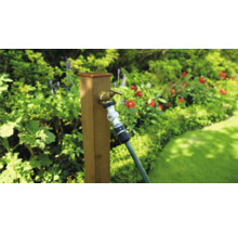 Tuinscene met kraan en tuinslang aan een houten paal