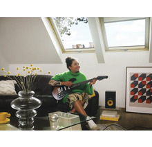 Vrouw speelt gitaar in een lichte woonkamer met dakramen