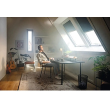 Een zolderkamer met dakramen, waar een man aan een bureau zit en naar muziek luistert.