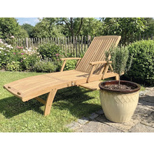 Houten tuinligstoel naast een pot met plant in de tuin