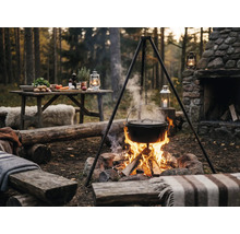 Buitenscène met driepoot, kookpot boven kampvuur en tafel met ingrediënten