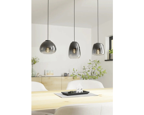 Drie glazen hanglampen boven een houten tafel in een lichte ruimte