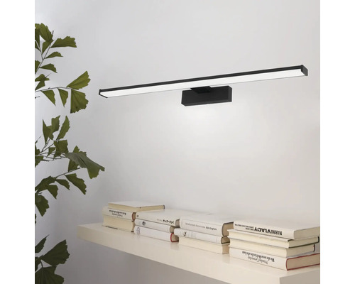 Wandlamp met strak design boven een plank met boeken en een plant.