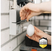 Iemand steekt een stekker in een stopcontact. Home Defense Logo