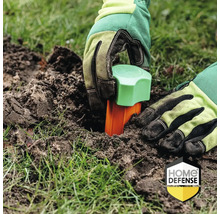 Een persoon plaatst met handschoenen een woelmuisblokkade in de grond.