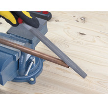 Een koperen buis wordt bewerkt met een vijl, die in een bankschroef is bevestigd.