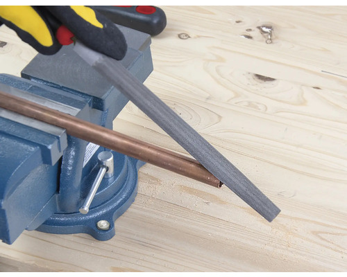 Een koperen buis wordt bewerkt met een vijl, die in een bankschroef is bevestigd.