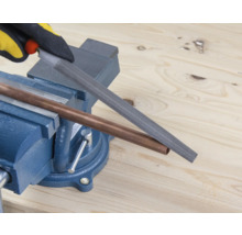 Een koperen buis wordt bewerkt met een vijl die in een bankschroef is geklemd.