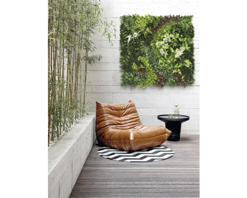 Scène met een fauteuil, een tafel, een rond tapijt en een groen wandpaneel op een terras