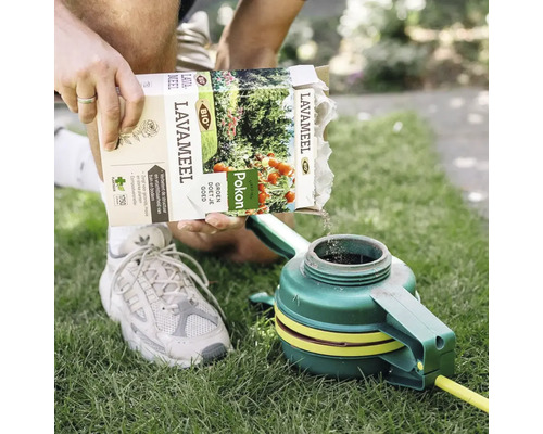 Persoon giet Pokon lavameel in een tuingereedschap op een gazon.