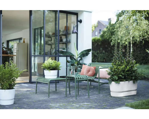 Modern terras met groene metalen tuinbank, bijzettafels en witte bloempotten voor een glazen pui.