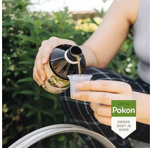 Een persoon giet vloeibare plantenvoeding uit een Pokon fles in een maatbeker in een tuin. Pokon Logo.