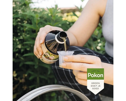 Een persoon giet vloeibare plantenvoeding uit een Pokon fles in een maatbeker in een tuin. Pokon Logo.