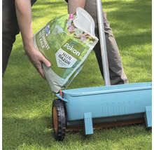 Een persoon vult een blauwe strooiwagen met Pokon Gazonmest met kalk vanuit een zak op een gazon.