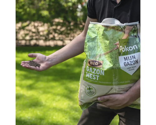 Persoon houdt een zak Pokon Bio Gazonmest vast en toont korrels in de hand op een gazon.