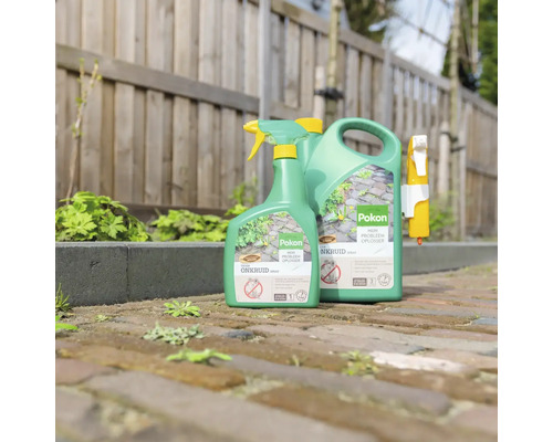 Pokon onkruidspray in spuitfles en jerrycan op een klinkerpad voor een houten schutting.