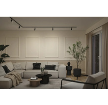 Moderne woonkamer met zwart railsysteem aan het plafond, een grote lichte hoekbank en minimalistische wanddecoratie.