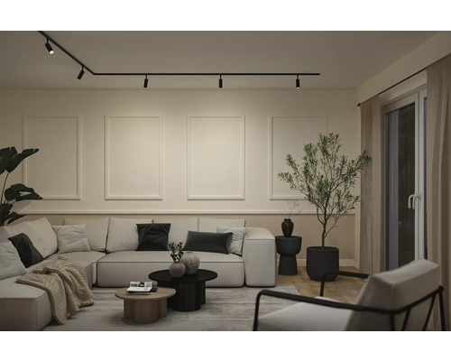 Moderne woonkamer met zwart railsysteem aan het plafond, een grote lichte hoekbank en minimalistische wanddecoratie.