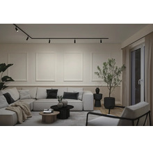 Moderne woonkamer met railsysteem aan het plafond, wandlijsten, grote hoekbank, salontafels en een kamerplant.
