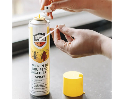 Handen bevestigen een precisiespuitmond aan een Home Defense Cure spuitbus tegen mieren en kruipend ongedierte.