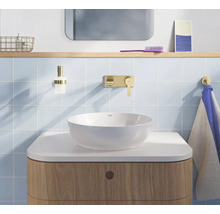 Lichte badkamer met witte opbouwkom, gouden wandkraan, houten onderkast en lichtblauwe tegels.