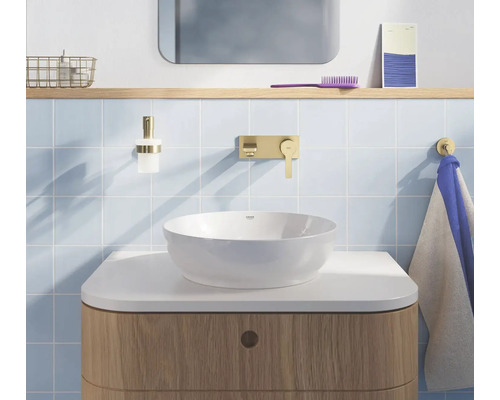 Lichte badkamer met witte opbouwkom, gouden wandkraan, houten onderkast en lichtblauwe tegels.