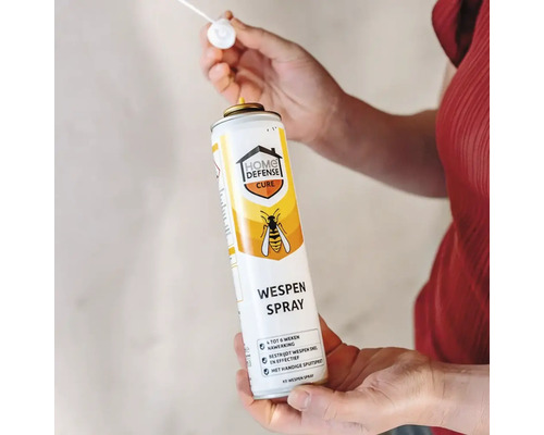 Persoon houdt een spuitbus Home Defense Cure wespenspray vast met een precisienozzle voor insectenbestrijding.