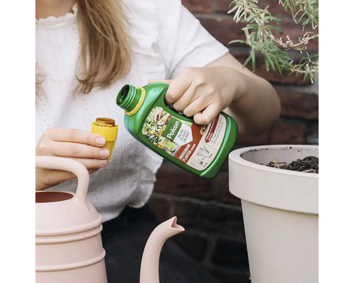 Iemand schenkt Pokon Mediterrane Planten Voeding in een doseerdop naast een plantenpot en een gieter.