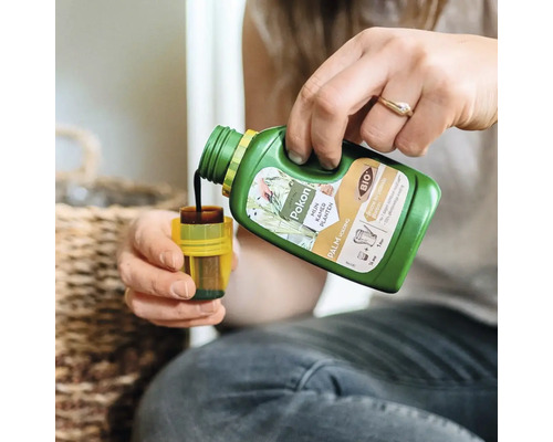 Een persoon schenkt vloeibare Pokon Bio palmvoeding uit een groene fles in een gele doseerdop.