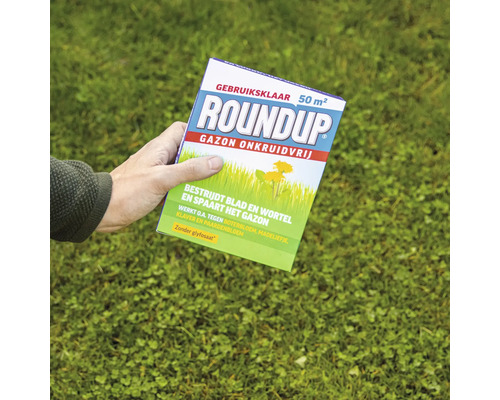 Een persoon houdt een verpakking Roundup Gazon Onkruidvrij onkruidverdelger voor 50 vierkante meter boven een grasveld vast.