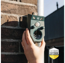 Een hand houdt een groene KB ultrasone dierenverjager tegen een bakstenen muur. Home Defense Logo.