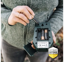 Plaatsen van een AA-batterij in het open batterijcompartiment van een groene katten- en hondenverjager. Home Defense Logo.