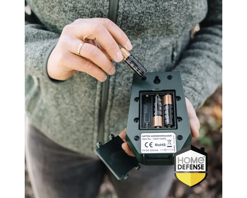 Plaatsen van een AA-batterij in het open batterijcompartiment van een groene katten- en hondenverjager. Home Defense Logo.