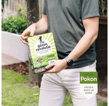 Een persoon houdt een verpakking Pokon Gazon Revolutie graszaad vast in een tuin.