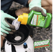 Een persoon giet Roundup onkruidverdelger concentraat in een maatbeker boven een drukspuit. Roundup Logo.