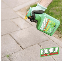 Hand met werkhandschoen spuit Roundup Totaal onkruidverdelger op voegen tussen stoeptegels.