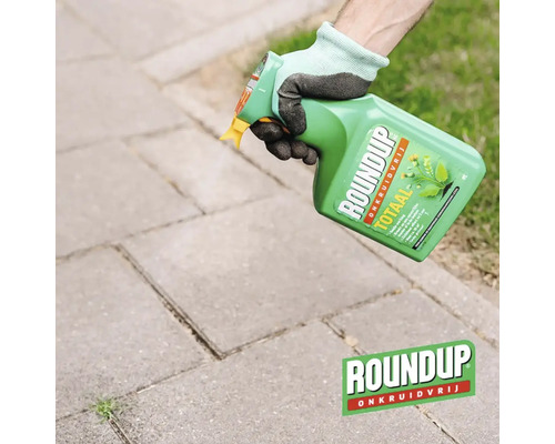 Hand met werkhandschoen spuit Roundup Totaal onkruidverdelger op voegen tussen stoeptegels.