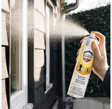 Hand spuit Home Defense Cure insectenspray tegen vliegen en muggen op een buitenmuur.