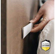 Een hand brengt een plakstrip aan op een houten oppervlak. Home Defense Logo.