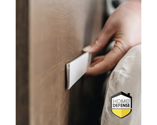 Een hand brengt een plakstrip aan op een houten oppervlak. Home Defense Logo.