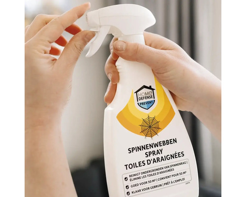 Handen houden een spuitfles Home Defense spinnenraggenspray vast voor het reinigen van oppervlakken van spinnenrag.